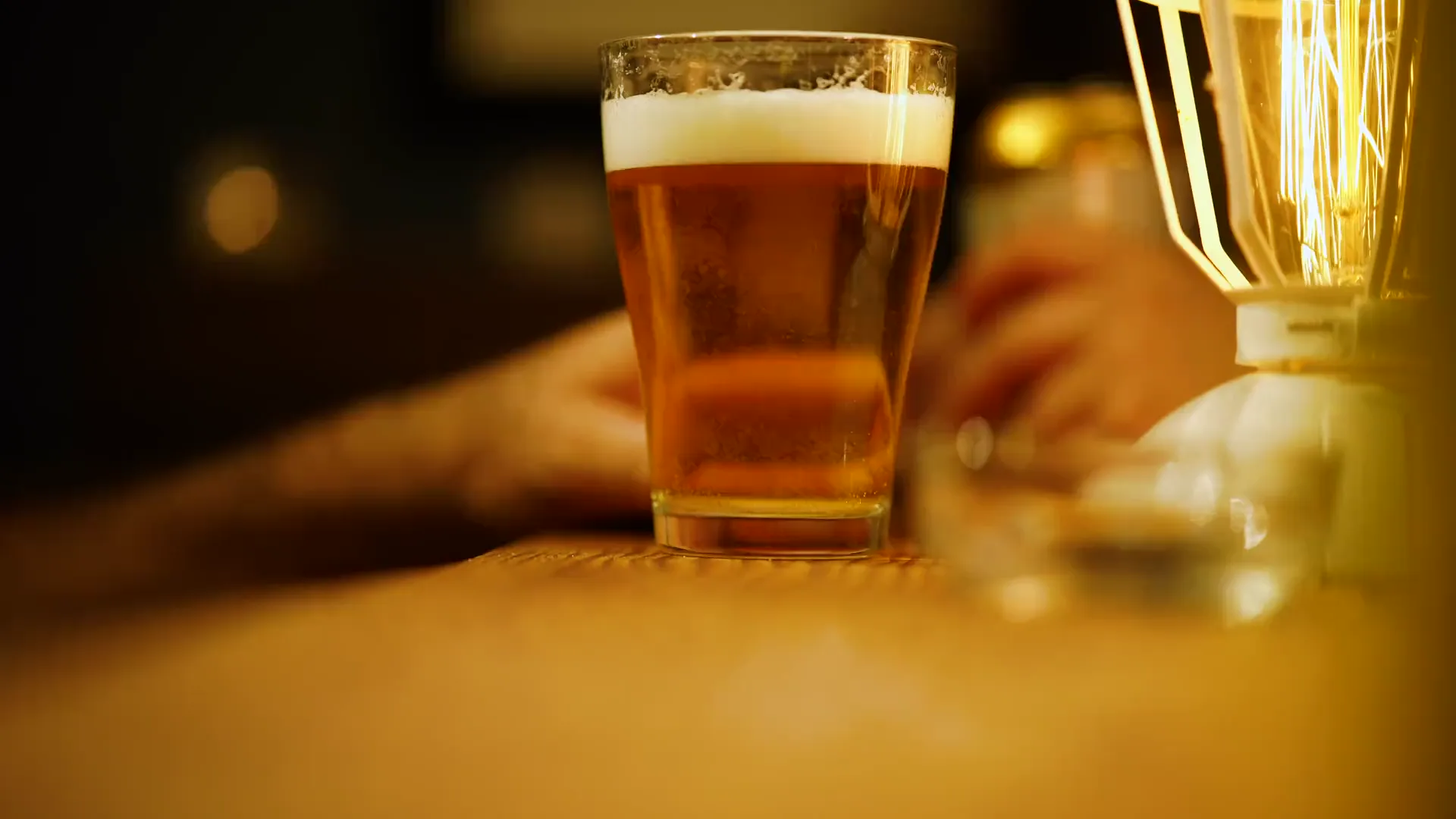 Bancone di un locale la sera, una birra appena spillata e una lampadina a filamento